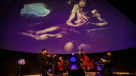 Grupo de cuerda tocando, tras ellos una proyección de un cuadro de El Prado.