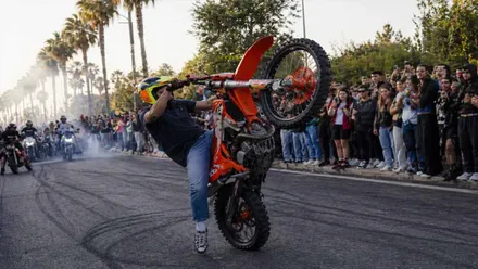 Momento en el que un motorista hace el caballito con una motocicleta de cross en color naranja.