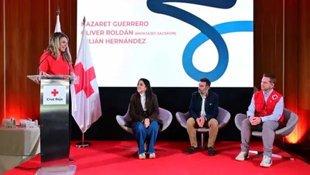 Cuatro personas en un escenario en el que una miembro de la Cruz Roja presenta a los galardonados.