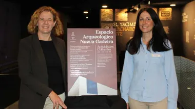 Cartel con las actividades en Nueva Gadeira, la delegada y la responsable posan junto al mismo.