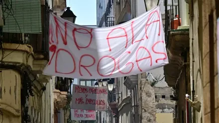 Una gran pancarta blanca con letras rojas y el mensaje "No a las drogas" cuelga entre los edificios de una estrecha calle del barrio de Santa María, en Cádiz. Al fondo se observan otras pancartas reivindicativas, entre ellas una con el lema "Menos papelinas y más papelillos".
