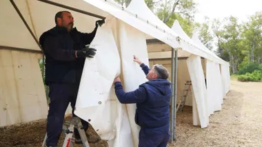 Dos operarios rematan una cortina color beige de una carpa.