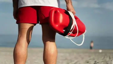 Socorrista con el flotador, camiseta blanca y bañador rojo típico.