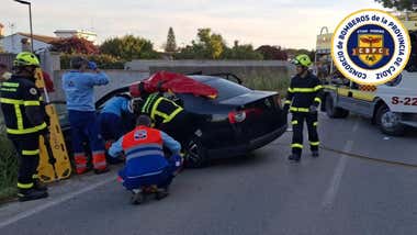 Coche siniestrado en color oscuro y bomberos trabajando para sacar a las mujeres.