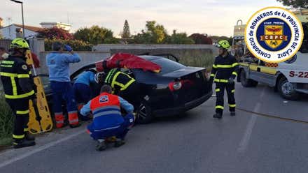 Coche siniestrado en color oscuro y bomberos trabajando para sacar a las mujeres.