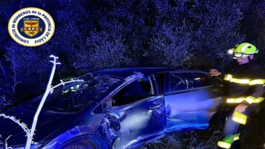 Coche accidentado de color metalizado y un bombero a su lado.
