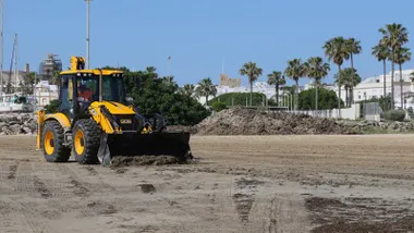 Excavadora de color amarillo retirando algas invasoras de una playa roteña.
