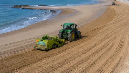 Un tractor de color verde rearenando la playa.