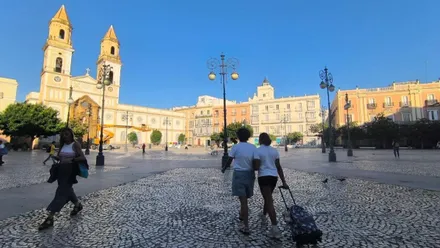 Varias personas caminas por la plaza de San Antonio de Cádiz, con maquinaria de reformas de la iglesia al fondo y un cielo azul
