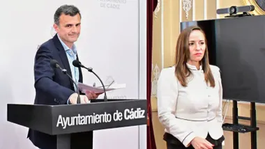 Virginia Martín y Bruno García aparecen de pie durante una comparecencia institucional en dependencias municipales. Ambos miran hacia los asistentes mientras intervienen en un acto público relacionado con la actividad del Ayuntamiento de Cádiz. Al fondo se observan elementos identificativos del Consistorio.