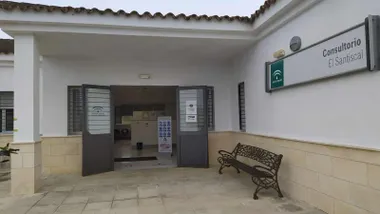 Edificio del Consultorio Médico de la Sierra de Cádiz, tiene un banco bajo el cartel del mismo y la puerta de entrada.
