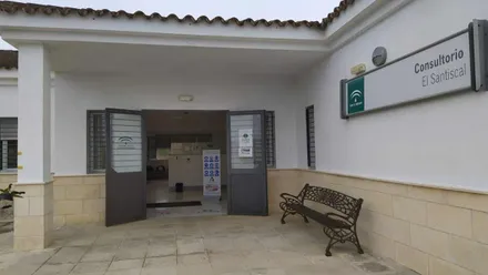 Edificio del Consultorio Médico de la Sierra de Cádiz, tiene un banco bajo el cartel del mismo y la puerta de entrada.