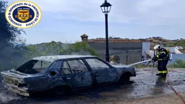 Coche completamente quemado siendo sofocado el incendio por un bombero.