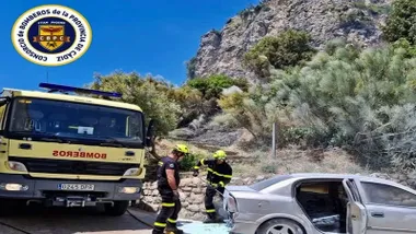 Dos bomberos junto a un vehículo en labores de sofocar un incendio.
