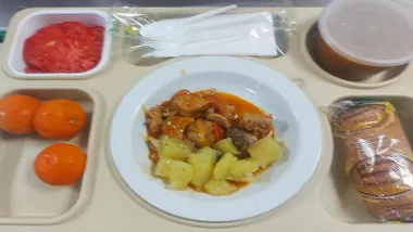 Plato con guiso y fruta más una pieza de pan.