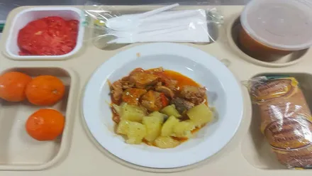 Plato con guiso y fruta más una pieza de pan.