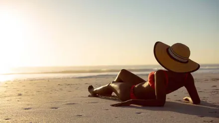 Mujer con bikini y pamela tomando el sol en la orilla de la playa.