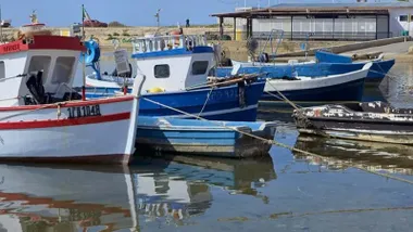 Atracados en el muelle diferentes barcas y barcos pesqueros en vistosos colores blancos y azules.