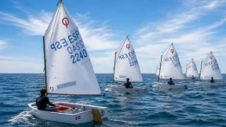 Pequeños barcos de clase Optimist en una competición sobre aguas muy azules.