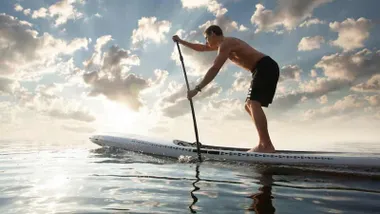 Chico subido sobre una tabla de surf y avanzando con una pala.