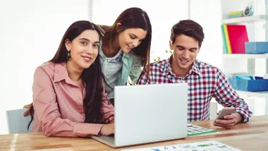 Dos chicas y un chico mirando a la pantalla de un portatil.