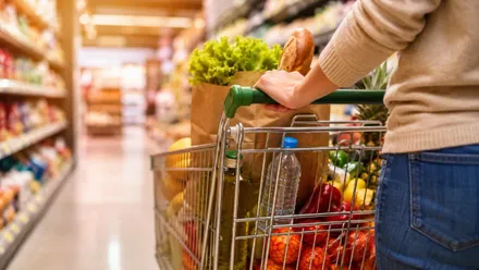Mujer empujando un carro de la compra lleno en un supermercado.