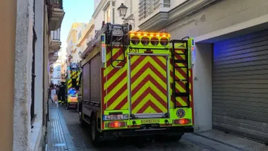 Dos camiones de bomberos, en rojo y amarillo, con las luces encendidas. Es una calle estrecha.