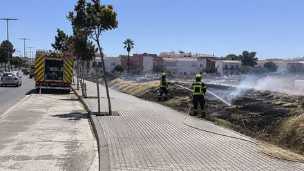 Dos bomberos extinguen un incendio de pastos a pie de carretera en San Fernando. Hay zona quemada.