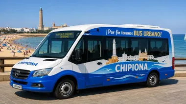 Autobús en blanco y azul y de fondo el faro de Chipiona y la playa.