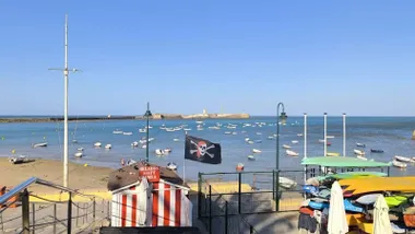 Bandera movida intensamente por el viento en la Playa de la Caleta de Cádiz durante un episodio de Levante con avisos amarillos activos por rachas fuertes y fenómenos costeros.