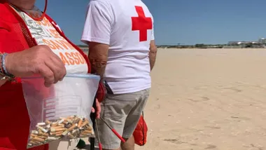 Dos miembros de la Cruz Roja recogiendo colillas en la playa.