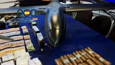 Mesa con fondo azul en el que hay un dron de color negro, fajos de billetes y droga.