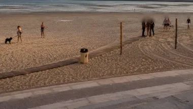Playa con personas y dos policías con el detenido, es el caer del sol.