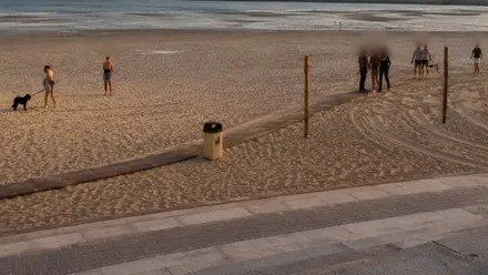 Playa con personas y dos policías con el detenido, es el caer del sol.