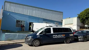 Nave con techo de metálico y furgón de la Policía Nacional aparcado en la entrada.