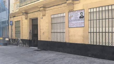 Imagen de la fachada de un edificio histórico situado en la plaza de Viudas de Cádiz. En la pared exterior se aprecia una placa conmemorativa que recuerda el nacimiento de Fermín Salvochea en este inmueble. La finca presenta signos visibles de antigüedad y es objeto de debate por los problemas estructurales denunciados por sus residentes y por Adelante Izquierda Gaditana.