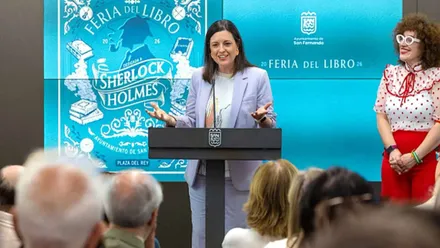 Patricia Cavada, de chaqueta azulona y tras ella el cartel de la Feria del Libro de San Fernando.