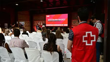 Carmen de Lara habla desde el atril durante la inauguración de la VII Feria de Empleo de Cruz Roja en Cádiz. Sentados a su lado se encuentran representantes de distintas administraciones públicas participantes en el acto, mientras decenas de asistentes siguen el evento en los antiguos Depósitos de Tabaco.
