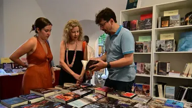 Librero mostrando libros a unas clientas en uno de los expositores de la 41ª Feria del Libro de Cádiz 2026 en el Baluarte de la Candelaria.