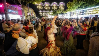 Calle muy iluminada y personas bailando sevillanas en la Feria de Puerto Real.