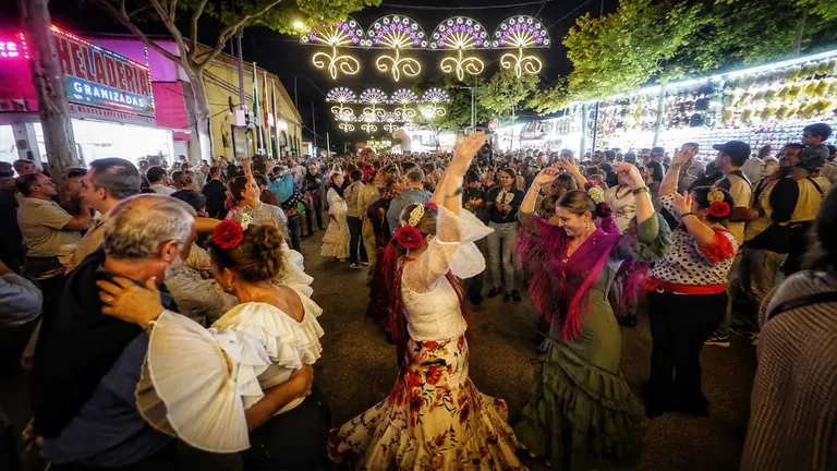 Calle muy iluminada y personas bailando sevillanas en la Feria de Puerto Real.