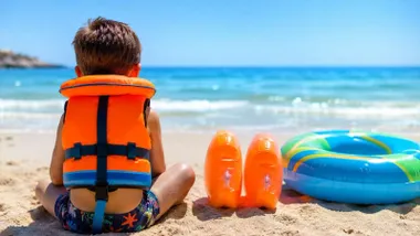 Niño en la orilla de la playa con flotadores.