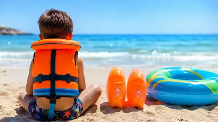 Niño en la orilla de la playa con flotadores.