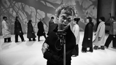 Imagen en blanco y negro de un cantante y, tras él, una serie de personas.