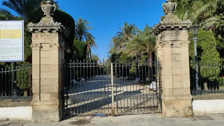 Acceso principal al Parque Genovés de Cádiz con las puertas cerradas durante un episodio de fuerte viento de Levante. El Ayuntamiento ha ordenado el cierre preventivo del recinto ante los avisos meteorológicos activos por rachas intensas de viento en la provincia.