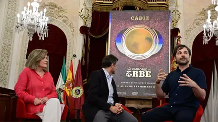 El alcalde Bruno García, Maite González y Alejandro Botubol junto al cartel oficial de ‘Emporio del orbe’, con la obra en el Salón de Plenos del Ayuntamiento de Cádiz como escenario de la presentación. Foto: Eulogio García.