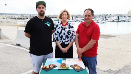 Tres personas ante platos con atún y, a su espalda, el puerto con los barcos recreativos.