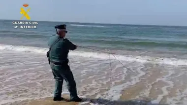Playa en la que hay un agente de la Guardia Civil tirando de una red.