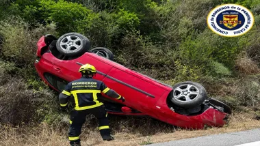 Vehículo rojo volcado con un bombero trabajando.