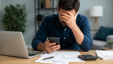Hombre con la mano en la cara mientras mira un teléfono móvil.